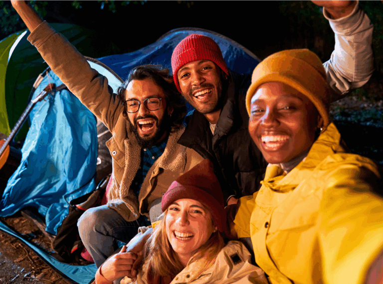 Group of young adults smiling around a tent at night during a camping trip, symbolizing connection and shared psychedelic experiences such as using magic mushrooms.