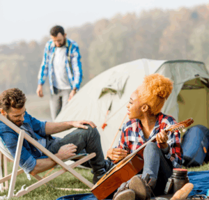 Young adults enjoy a relaxed camping experience in nature, playing music and lounging outside a tent, potentially representing a mellow setting related to sleep and shroom use.