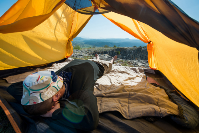 Person relaxing inside a tent with a scenic mountain view, wearing a colorful hat, representing a tranquil