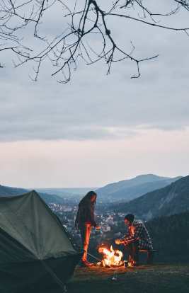 Couple enjoying a campfire on a hilltop at sunset with a tent pitched nearby – Good Friday Wellness magic mushroom delivery.
