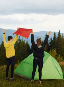Two hikers raising arms near a tent in the mountains — Good Friday Wellness magic mushroom capsules.