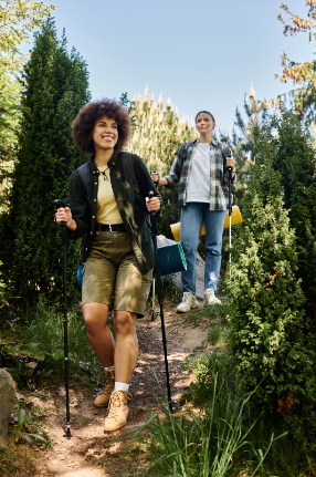 Two women hiking through a quiet forest trail at sunset, wearing warm clothing