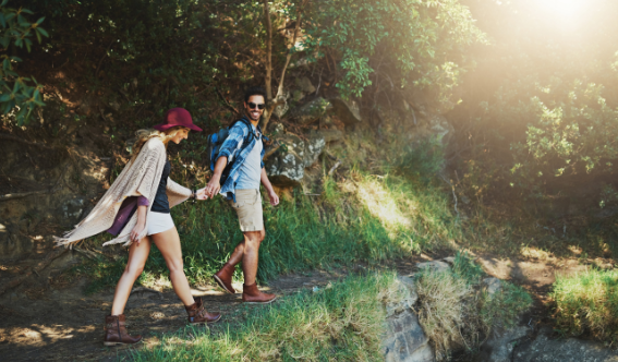 Couple hiking through sunlit forest trail while holding hands