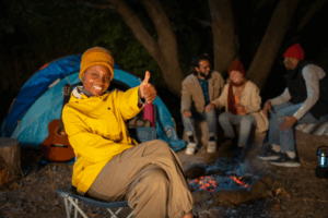Woman giving a thumbs up near a campfire with friends, embodying the joy of Good Friday Wellness magic mushroom capsules.