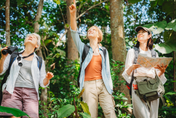Three women exploring the forest trail with map and binoculars.