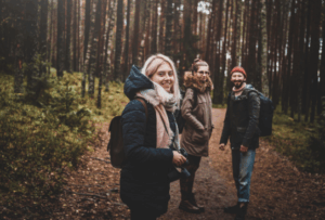 Three smiling friends stand in a forest clearing with backpacks, enjoying a hike through the woods, reflecting the natural spirit of Good Friday Wellness Psilocybin Magic Mushrooms