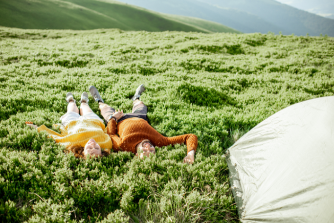 Couple lying on green hillside near tent enjoying nature