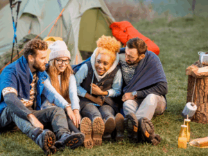 Friends bundled in warm layers outside a tent, sharing laughter and warmth on a camping trip