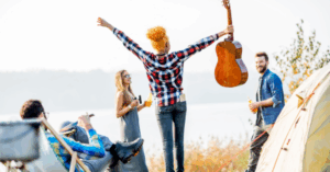 Woman holding guitar and celebrating near campsite with friends, inspired by Good Friday Wellness magic mushrooms