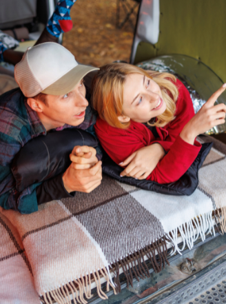 Couple relaxing in a cozy camper setup during a nature trip, smiling and pointing at the sky.