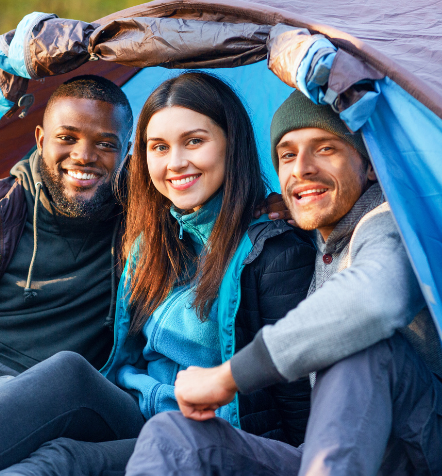 Three friends smiling and sitting inside a tent during a camping trip, representing a joyful moment enhanced by Good Friday Wellness magic mushroom delivery.