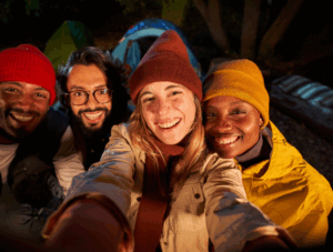 Friends smiling around a campfire with tents in the background, enjoying nature with Good Friday Wellness magic mushroom delivery Canada.