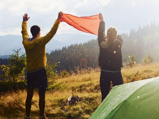 Two hikers holding a red cloth in the sunlight with mountains behind
