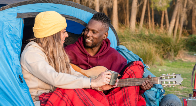 Couple enjoying a cozy moment camping with guitar and drinks