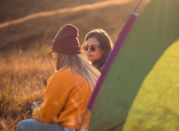 Two women relaxing by a tent during golden hour with Good Friday Wellness magic mushrooms