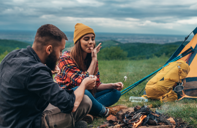 Couple enjoying a campfire on a hillside with backpack and tent nearby – Good Friday Wellness magic mushroom delivery