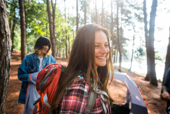 Smiling woman near forest tent with backpack – Good Friday Wellness Psilocybin Magic Mushrooms