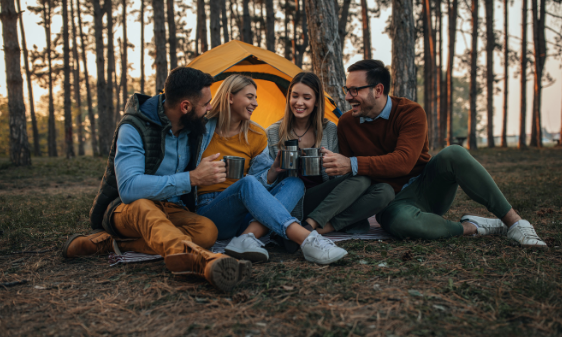 Group of friends drinking together by a tent in the forest.
