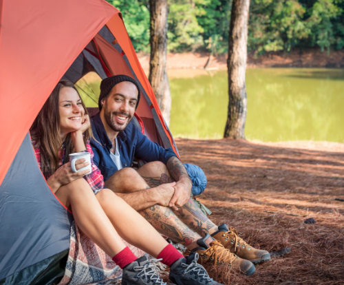 Couple smiling while sitting inside an orange tent near a forest lake – Good Friday Wellness Psilocybin Magic Mushrooms