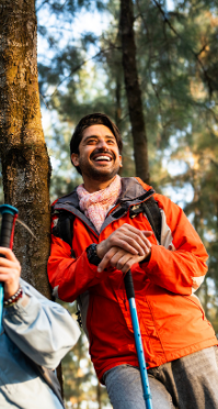 A joyful hiker in an orange jacket leaning on a walking stick, enjoying nature with the help of Good Friday Wellness magic mushroom delivery.