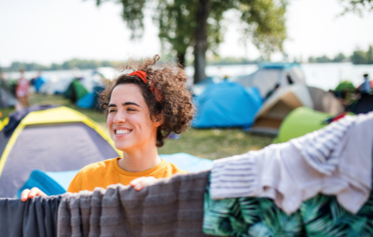 Smiling woman standing near a line of laundry at a vibrant lakeside campsite, surrounded by colorful tents