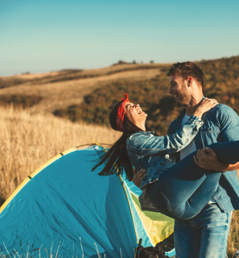 Couple smiling at a scenic campsite near a blue tent, symbolizing joy and connection enhanced by Good Friday Wellness magic mushroom delivery.