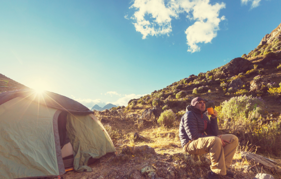 Man enjoying sunrise near tent with coffee, embracing nature and Good Friday Wellness Psilocybin Magic Mushrooms experience.