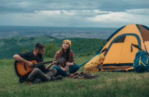 Couple camping on a mountain with arms raised, celebrating the moment with Good Friday Wellness magic mushroom capsules.