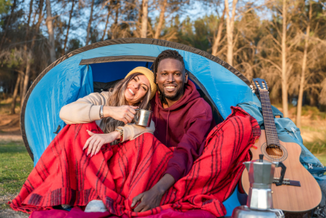 Happy couple enjoying a camping morning outside a tent with a guitar and thermos nearby