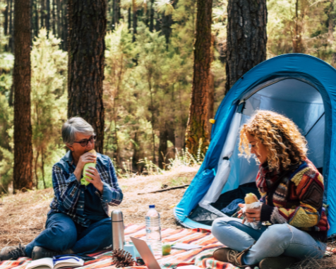 Two women enjoy a peaceful forest camping moment with food and drinks near a tent