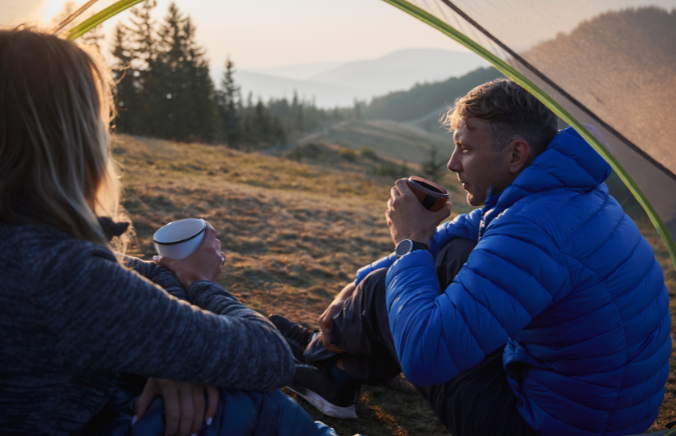 Couple sitting inside a tent at sunrise with hot drinks
