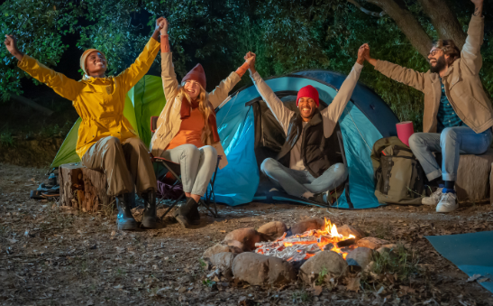 Group of friends holding hands around a campfire with tents in the background