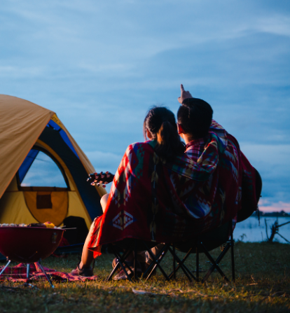 Couple stargazing by a tent at dusk with guitar