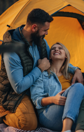 Couple smiling and cuddling outside a tent during a camping trip, promoting Good Friday Wellness Psilocybin Magic Mushrooms.