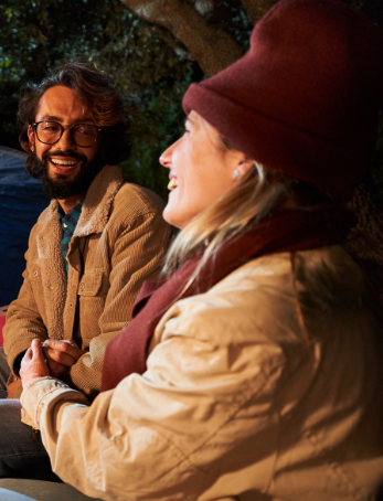 Two friends smiling by the campfire, enjoying nature and each other's company