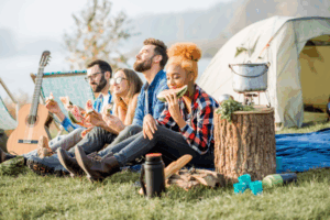 Group of friends relaxing and eating watermelon outside tents during a camping trip, associated with Good Friday Wellness Psilocybin Magic Mushrooms.