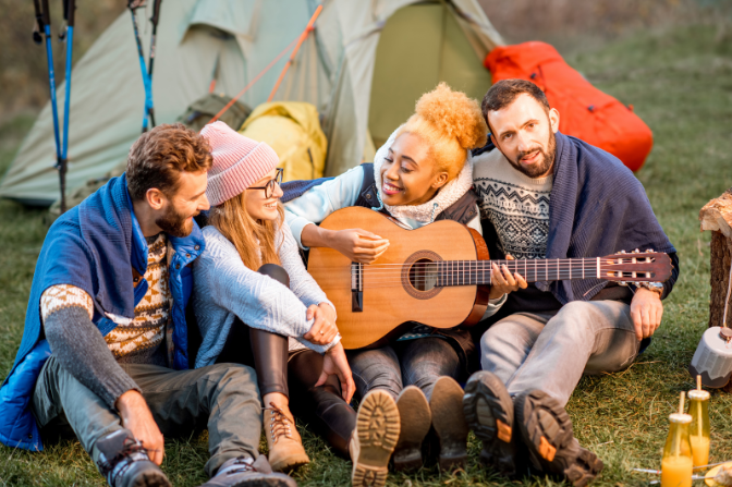 Group of friends sitting outside tents with a guitar, enjoying a camping experience associated with Good Friday Wellness magic mushroom delivery Canada.
