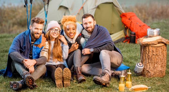 Happy group of campers posing on a grassy field with a tent in the background.